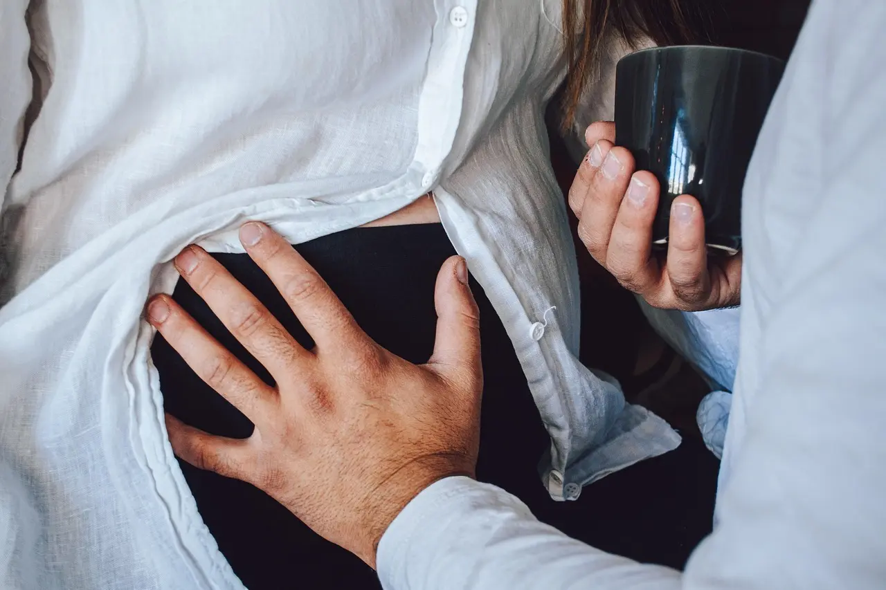 Hænder på en mave og en person der holder en kop